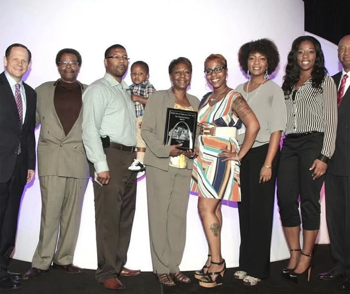 Group of people posing formally at an event, with one person holding a recognition plaque.