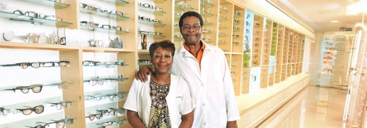 The founders of Eye Fashion Factory in lab coats standing inside a well‑organized optical showroom.