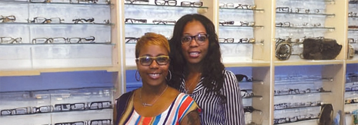 Two individuals inside an optical shop, surrounded by neatly organized displays of eyeglass frames.