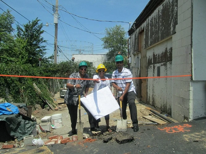 The founders of Eye Fashion Factory in safety helmets reviewing construction plans at an outdoor job site.