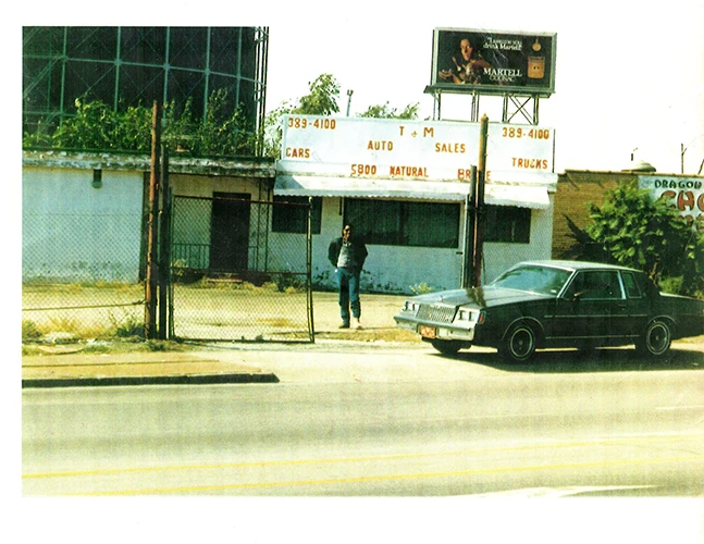 Small auto sales lot with a parked car, gated entrance, and an older commercial building.
